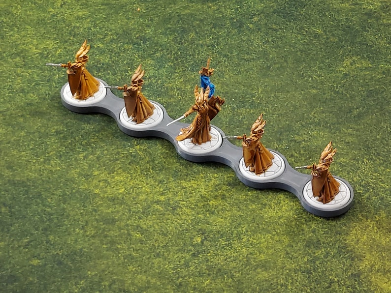 May include: Five gold-painted miniature figures of women wearing flowing robes and holding swords, standing on a grey and white plastic base with a connected design.