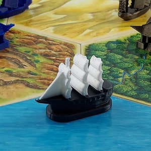 May include: A black and white miniature ship with white sails. The ship is sitting on a blue surface.