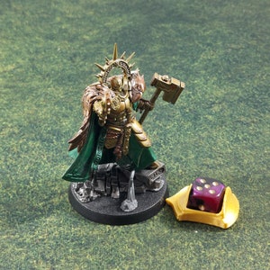 May include: A gold and green miniature figure of a warrior holding a hammer, standing on a black base with a stone texture. A purple and black dice is on a gold base.
