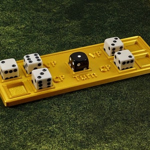 May include: A gold-colored game board with five dice. Four of the dice are white with black dots, and one is black with white dots. The board has the words "Turn", "CP", "VP", and "CF" printed on it.