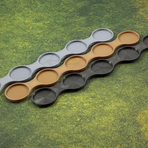 May include: Three sets of connected circular trays in grey, brown, and black. The trays are designed to hold miniature figures or other small objects.