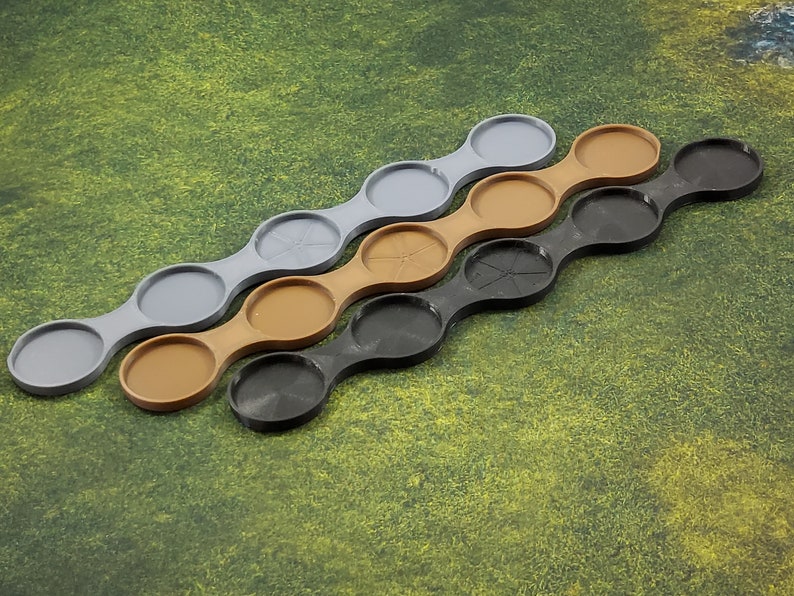May include: Three sets of connected circular trays in grey, brown, and black. The trays are designed to hold miniature figures or other small objects.