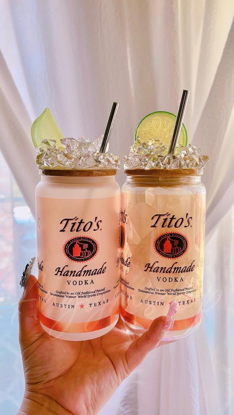 K&ouml;nnte beinhalten: Zwei durchsichtige Glaskanister mit Deckeln, gef&uuml;llt mit Eis und Limettenspalten. Die Kanister sind mit "Tito's Handmade Vodka" beschriftet, wobei am unteren Rand "Austin Texas" steht.