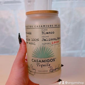 Puede incluir: Un vaso de vidrio esmerilado con tapa de bamb&uacute; y una pajita. El vaso tiene una etiqueta de tequila Casamigos con el texto "Clase Blanco", "Hecho Jalisco, M&eacute;xico", y "Numero 23044". La etiqueta tambi&eacute;n presenta un gr&aacute;fico de planta de agave verde y el logotipo de Casamigos.