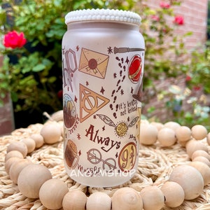 Op de afbeelding: Witte keramische pot met een witte parelmoerachtige rand. De pot heeft een Harry Potter-thema met verschillende illustraties, waaronder het Hogwarts-wapen, een gouden snitch, een brief en de woorden "Always" en "9 3/4".