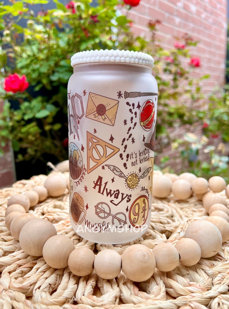 Op de afbeelding: Witte keramische pot met een witte parelmoerachtige rand. De pot heeft een Harry Potter-thema met verschillende illustraties, waaronder het Hogwarts-wapen, een gouden snitch, een brief en de woorden "Always" en "9 3/4".