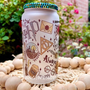 Op de afbeelding: Een witte, gematteerde glazen fles met een groene ritsteenklep. De fles is versierd met een Harry Potter-thema, waaronder het Hogwarts-wapen, een gouden snitch en de woorden "Always".