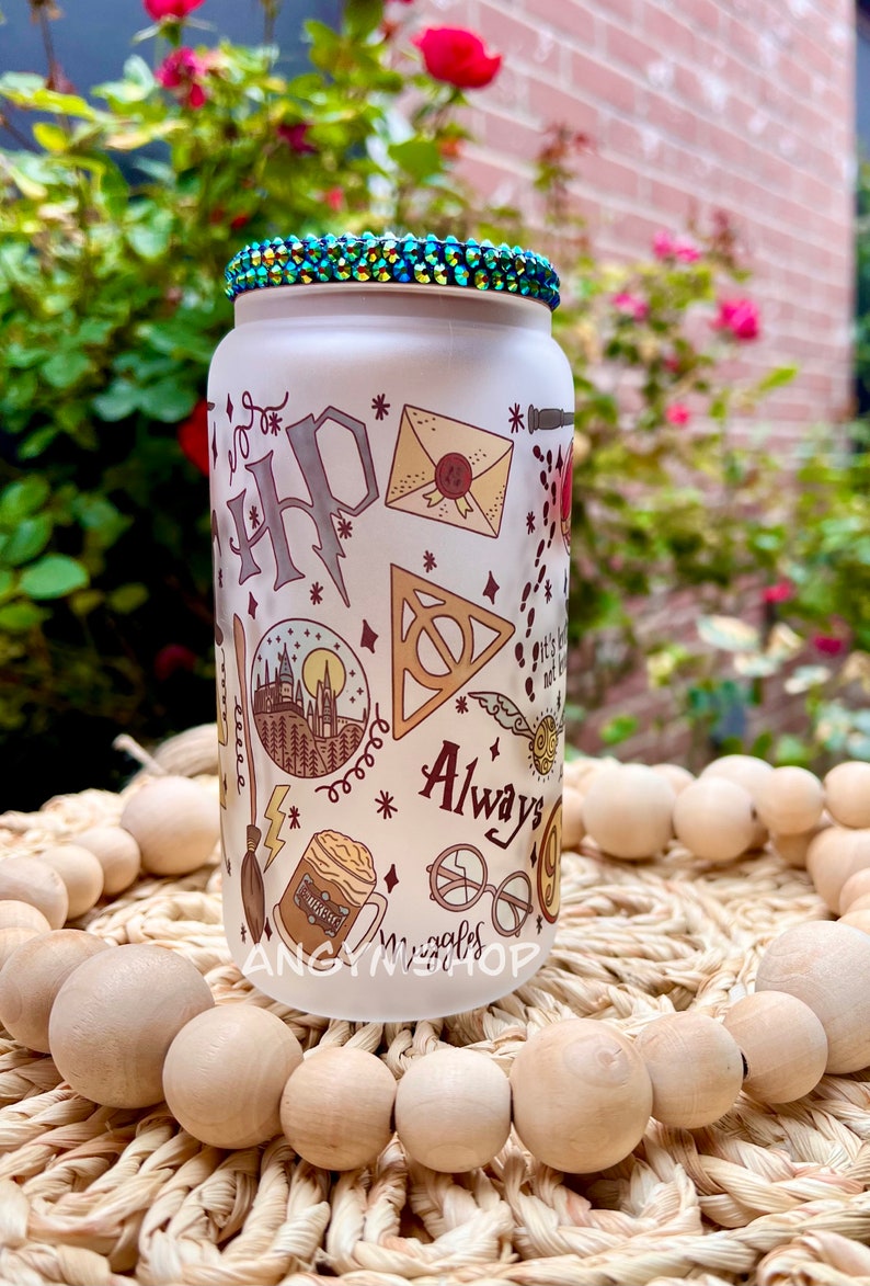 Op de afbeelding: Een witte, gematteerde glazen fles met een groene ritsteenklep. De fles is versierd met een Harry Potter-thema, waaronder het Hogwarts-wapen, een gouden snitch en de woorden "Always".