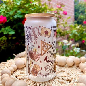 Op de afbeelding: Een witte, gematteerde glazen pot met een bamboe deksel met een Harry Potter-thema. De pot is versierd met illustraties van het kasteel van Zweinstein, het symbool van de Doodsgeesten, een bliksem, een gouden snitch, een rond brilletje, een Zweinstein-brief en de woorden "Always".