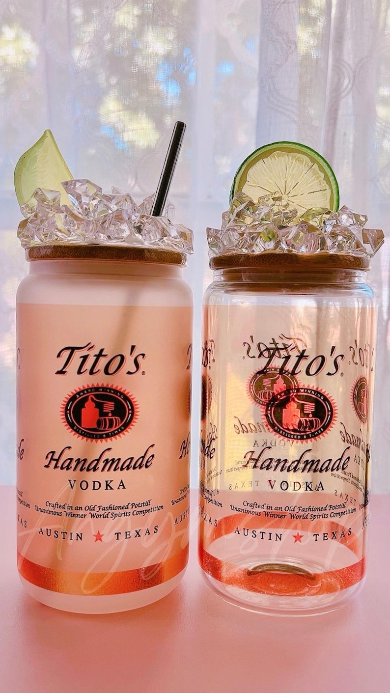 K&ouml;nnte beinhalten: Zwei durchsichtige Glasbeh&auml;lter mit braunem Deckel und wei&szlig;em Etikett. Das Etikett tr&auml;gt den Schriftzug "Tito's Handmade Vodka" mit einem roten Logo und dem Text "Crafted in an Old Fashioned Potstill Unanimous Winner World Spirits Competition Austin Texas".