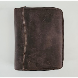 May include: A dark brown leather zippered portfolio case with a distressed finish. The front panel features a vertical decorative stitched seam running along the left side, and the entire rectangular organizer is secured with a matching zipper.