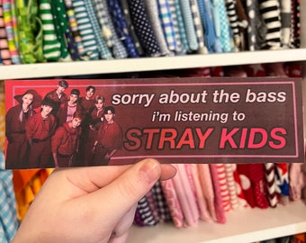 Może przedstawiać: Naklejka w kolorze czerwonym i czarnym z tekstem "sorry about the bass i'm listening to STRAY KIDS". Naklejka zawiera zdjęcie grupy osób ubranych na czerwono.