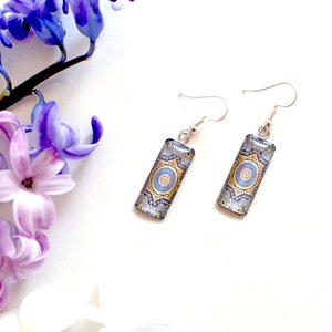 May include: A pair of silver dangle earrings with rectangular blue, yellow and orange patterned charms.