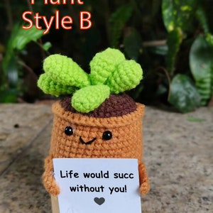 May include: A crocheted plant pot with a green plant and a sign that reads "Life would succ without you!" The pot has a smiling face and black eyes.