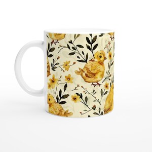 May include: White ceramic mug with a yellow chick and floral pattern. The chick is surrounded by yellow flowers and green leaves.