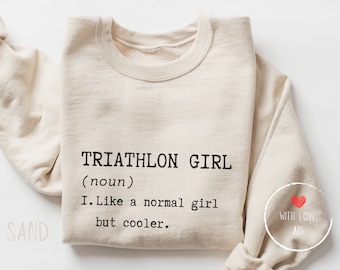 May include: A beige sweatshirt with the text "TRIATHLON GIRL (noun) I. Like a normal girl but cooler." printed on the front. The text is in black and the sweatshirt has a distressed look.