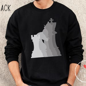 Può includere: Felpa nera con una silhouette grigia di pezzi degli scacchi, tra cui un re, una regina, una torre e un pedone.