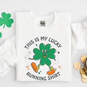 May include: White sweatshirt with a green four-leaf clover graphic and the text "This is my lucky running shirt".