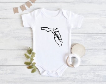 May include: White baby onesie with a black outline of the state of Florida and the word "home" written in cursive inside the state.