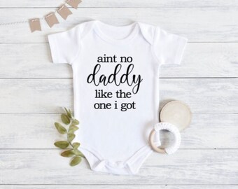 May include: White baby onesie with black text that reads "ain't no daddy like the one i got".