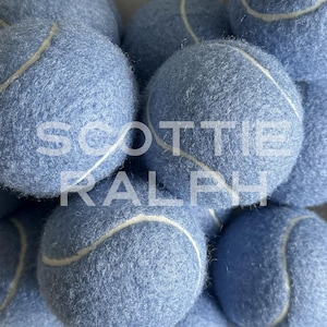 May include: A collection of light blue tennis balls with a fuzzy texture and white seams. The text "SCOTTIE RALPH" is overlaid in white capital letters across the centre of the image, partially obscuring the surface of the blue tennis balls.