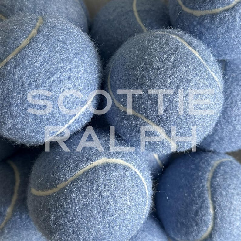 May include: A collection of light blue tennis balls with a fuzzy texture and white seams. The text "SCOTTIE RALPH" is overlaid in white capital letters across the centre of the image, partially obscuring the surface of the blue tennis balls.