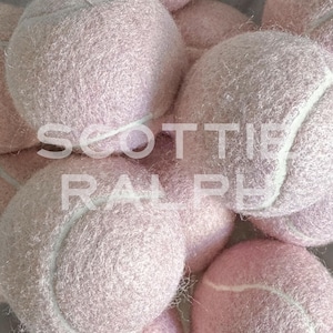 May include: A collection of fuzzy, light pink tennis balls with white seams. The text SCOTTIE RALPH is overlaid in white capital letters across the centre of the cluster of balls, which are arranged in a dense, overlapping pile.