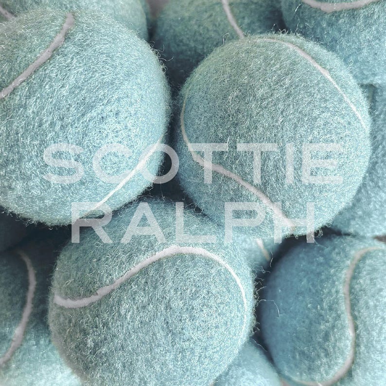 May include: A collection of fuzzy, light blue tennis balls with white seams. The text SCOTTIE RALPH is overlaid in white capital letters across the centre of the image, partially obscuring the textured surface of the spherical objects.