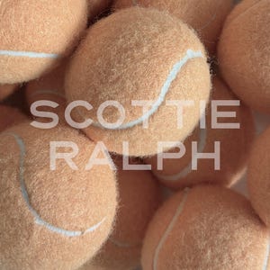 May include: A collection of fuzzy, light peach-coloured tennis balls with white seams. The text SCOTTIE RALPH is overlaid in white capital letters across the centre of the image, partially obscuring the textured surface of the round objects.