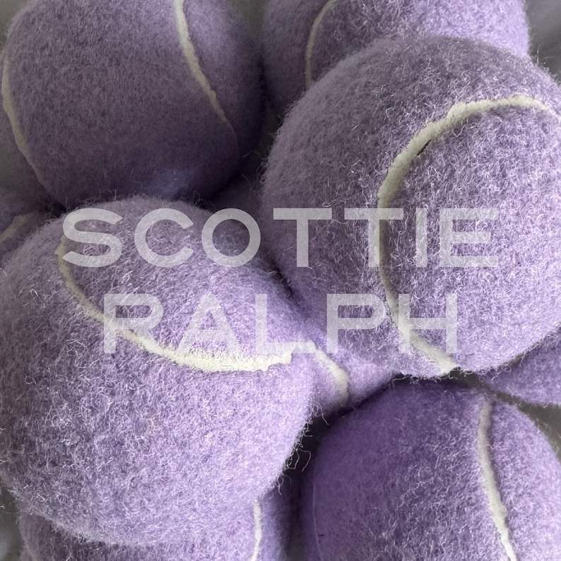 May include: A collection of fuzzy lavender tennis balls with white seams, arranged in a cluster. The text SCOTTIE RALPH is overlaid in white capital letters across the centre of the image, partially obscuring the textured surface of the balls.