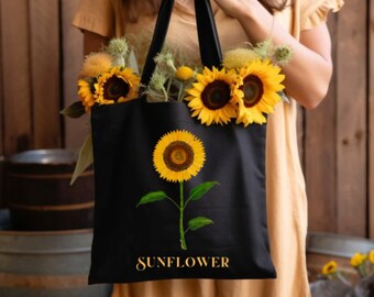 Peut inclure: Sac fourre-tout noir avec un motif de tournesol jaune et le mot "SUNFLOWER" en lettres dorées. Le sac est rempli de tournesols frais et d'autres fleurs jaunes. Le sac a des poignées noires.