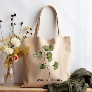 May include: A beige canvas tote bag with a green ginkgo biloba leaf design and the text "GINKGO BILOBA".