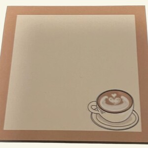 May include: Square coaster with a light beige center and a brown border. A coffee cup with latte art is in the lower right corner. The latte art is a heart shape.
