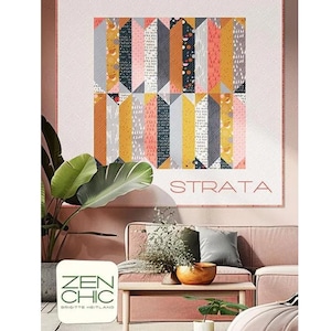 May include: A colorful quilt with a geometric design, featuring vertical stripes in shades of gray, yellow, orange, and pink. The word "STRATA" is displayed in a minimalist font. The quilt is displayed in a living room setting with a pink sofa and wooden coffee table.