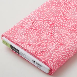 May include: A roll of hand-dyed fabric featuring a pink backdrop and a design of white, leaf-shaped motifs. The fabric is tightly rolled, with a label visible on the edge. The material is likely cotton or similar, ideal for quilting or sewing projects.