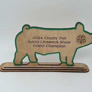 May include: Wooden pig silhouette award with a green outline. The award reads "2024 County Fair Junior Livestock Show Grand Champion" and features a 4-H clover.