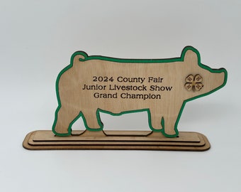 May include: Wooden pig silhouette award with a green outline. The award reads "2024 County Fair Junior Livestock Show Grand Champion" and features a 4-H clover.