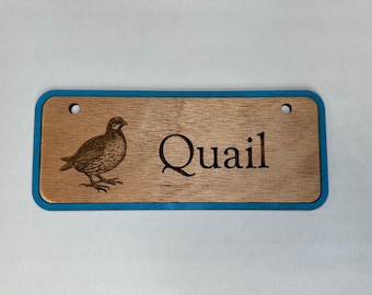 May include: A wooden sign with a blue border, featuring a laser-engraved image of a quail and the word "Quail".