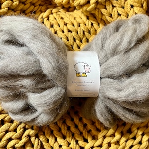 May include: A close-up of a bundle of gray Lincoln wool, with a white label that reads "Eph Jensen Livestock Woolworks Lincoln Wool" and a cartoon sheep wearing yellow boots.