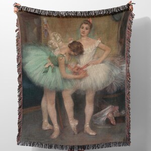 May include: Two ballerinas in a dance studio, one in a green tutu and the other in a white tutu, are adjusting their shoes. The ballerina in the green tutu is looking down at her shoes, while the ballerina in the white tutu is looking at the other ballerina. The background is a light brown color with a mirror on the left side of the image.
