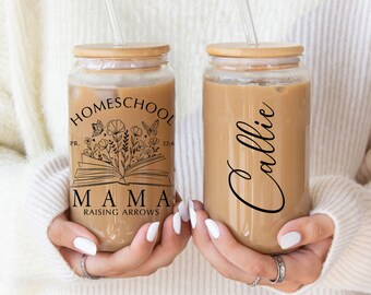 May include: Two clear glass tumblers with bamboo lids and reusable straws. One tumbler has the text "HOMESCHOOL MAMA RAISING ARROWS" with a book and floral design. The other tumbler has the name "Callie" written in cursive.