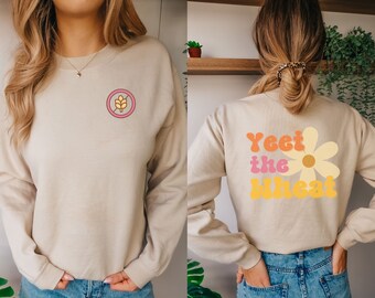 Könnte beinhalten: Ein beiger Pullover mit einem Grafikdruck einer Gänseblümchen und dem Text "Yeet the Wheat" auf der Rückseite. Die Vorderseite des Pullovers hat einen Grafikdruck eines Weizenährens mit einem diagonalen Strich durch.