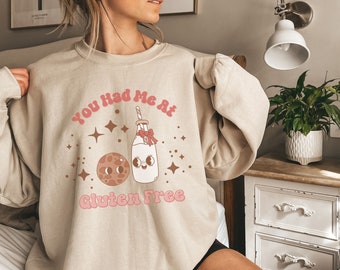 Könnte beinhalten: Ein beiger Pullover mit einem grafischen Design eines Kekses und einer Milchflasche mit dem Text "You Had Me At Gluten Free".