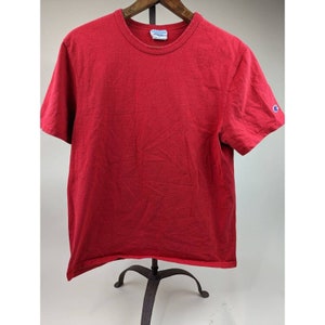 Puede incluir: Una camiseta roja de manga corta con un pequeño logotipo azul de Champion en la manga derecha.