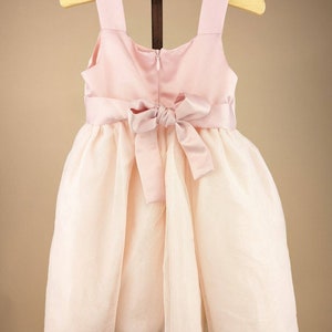 May include: A pink tulle dress with a satin bodice and a matching satin bow at the waist.