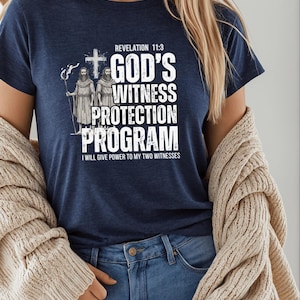 Pode incluir: Camiseta azul marinho com o texto branco "REVELATION 11:3 GOD'S WITNESS PROTECTION PROGRAM". A camisa apresenta uma ilustração de duas figuras e uma cruz. O texto "I WILL GIVE POWER TO MY TWO WITNESSES" também está incluído.