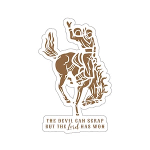 Könnte beinhalten: Eine braune Silhouette eines Cowboys, der einen buckelnden Bronco reitet, mit dem Text "THE DEVIL CAN SCRAP BUT THE Lord HAS WON".