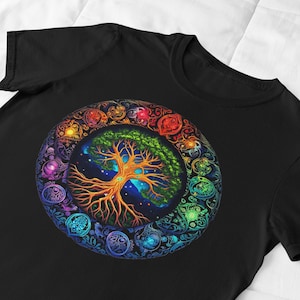 Pode incluir: Uma camiseta preta com um design colorido de árvore da vida. A árvore é cercada por um círculo de símbolos e desenhos coloridos.