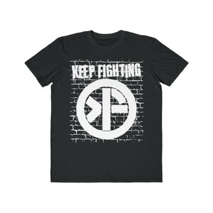May include: Black t-shirt with a white graphic of a circle with a symbol inside and the text "KEEP FIGHTING" on a brick wall background.