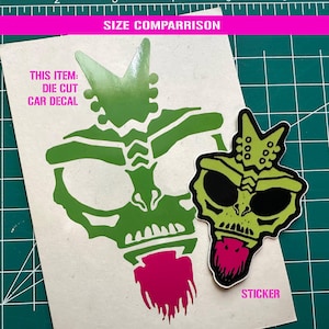 May include: A die-cut car decal and a sticker featuring a green and black skull design with a pink beard. The decal is larger than the sticker. The text "SIZE COMPARISON", "THIS ITEM: DIE CUT CAR DECAL", and "STICKER" are visible.